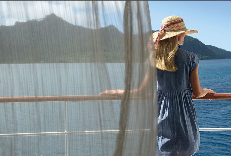 A woman in a sun hat enjoys the view and the fresh breeze on her balcony.