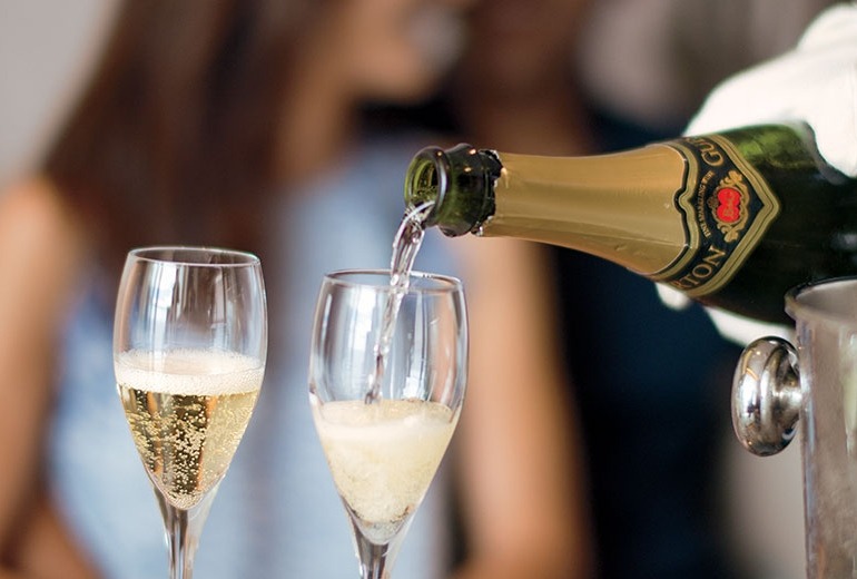 A white-gloved butler pours champagne for a couple in their suite.